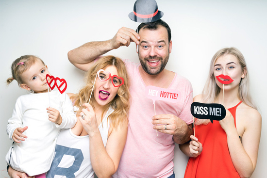 Family having fun with photo booth props, holding signs and wearing playful accessories