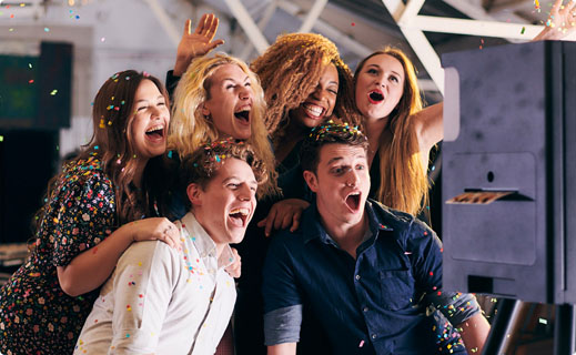 Group of friends excitedly using a photo booth, surrounded by confetti